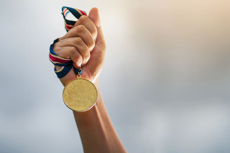 Una mano sostiene al aire una medalla de oro deportiva